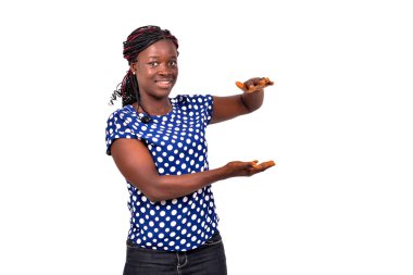 Güzel, mutlu genç bir kadının portresi beyaz arka planda duruyor ve elleriyle gülümseyerek bir şeyler gösteriyor..