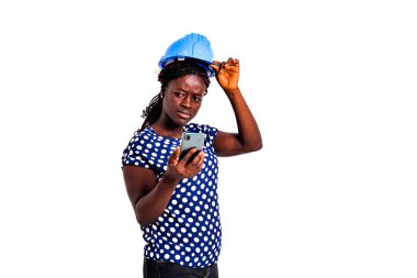 Güvenlik kasklı güzel bir bayan mühendis beyaz arka planda duruyor düşünceli bir bakışla cep telefonunu tutuyor..