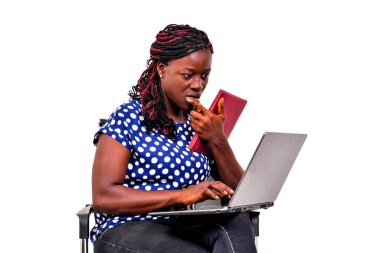 Evde bir sandalyede oturmuş dizüstü bilgisayar ve not defteri kullanarak çalışan güzel bir iş kadını..