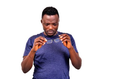 Beyaz arka planda duran mavi tişörtlü genç adam gözlüklere bakıyor..