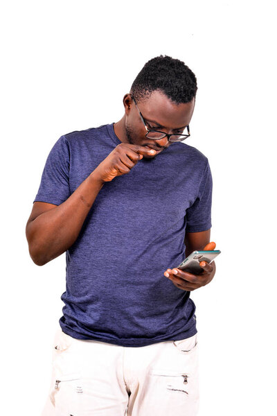 Young man in blue t-shirt standing on white background looking at cellphone and pointing finger.