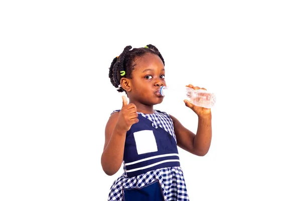 可愛い女の子は学校の服を着てペットボトルからミネラルウォーターを飲んで親指を見せて — ストック写真