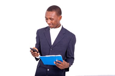 handsome businessman in jacket standing on white background holding notepad and looking at cellphone smiling.
