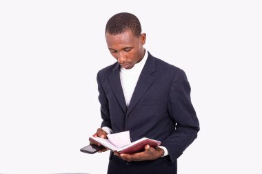 Yetişkin bir işadamı elinde cep telefonu tutarak defterini okuyor..