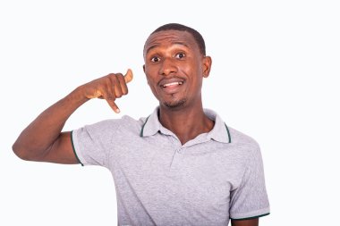 Beyaz arka planda duran gri tişörtlü genç bir adam telefon hareketlerini gösteriyor ve gülümseyen kameraya bakıyor..