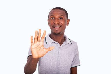 Beyaz arka planda duran gri tişörtlü genç adam avuç içini gösteriyor ve gülümseyen kameraya bakıyor..