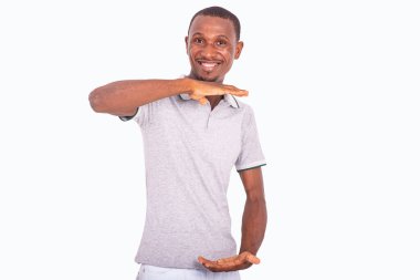 Beyaz arka planda duran gri tişörtlü genç adam gülümseyen bir şeyin büyüklüğünü gösteriyor..