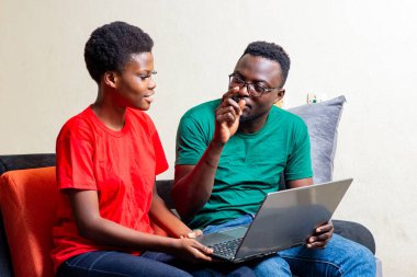 Güzel, genç bir Afrikalı çift evdeki kanepede dizüstü bilgisayar kullanarak oturuyor..