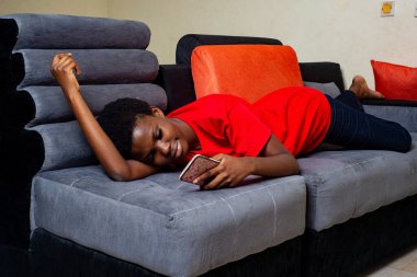 Evdeki kanepede uzanmış cep telefonuna gülümseyen güzel bir genç kız..