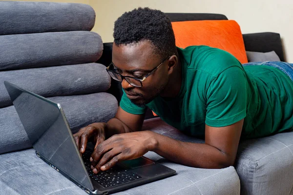 Młody Człowiek Okularach Optycznych Leżący Kanapie Domu Podczas Pracy Laptopem — Zdjęcie stockowe