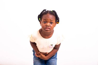 Beyaz arka planda durup karın ağrısından yakınan küçük şirin bir kız...