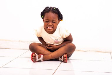 Kot pantolonlu güzel bir kız evde yerde oturup karın ağrısından yakınıyor..