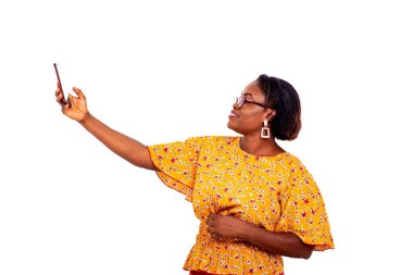 Beyaz arka planda duran gözlüklü güzel bir iş kadını cep telefonu kullanarak kendini fotoğraflıyor, gülümsüyor..