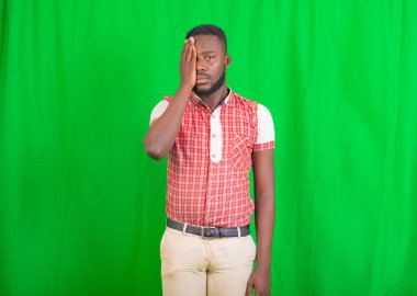 Yeşil arka planda duran ve bir gözünü kapatan yakışıklı bir gencin portresi..