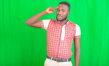 Yeşil arka planda duran yakışıklı bir gencin portresi. Alnında parmak olan bir şeyi düşünüyor..