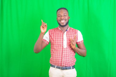 Yeşil arka planda duran ve işaret parmağıyla gülümseyen mutlu genç bir adamın portresi..