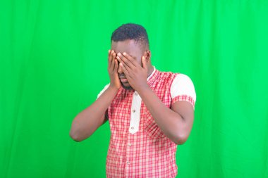 Yeşil arka planda duran yakışıklı bir gencin portresi ve her iki eli de yüzünde..