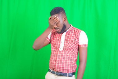 Yeşil arka planda duran ve elini alnına dayayan yakışıklı bir gencin portresi..