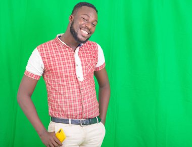 Yakışıklı, sakallı, elleri cebinde yeşil bir arka planda duran ve kameraya bakıp gülen bir adam..