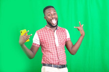 Yakışıklı, sakallı bir adam. Arka planda dikilip surat yapıyor..