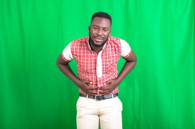 Yakışıklı, sakallı, yeşil arka planda duran ve midesinde ağrı hisseden bir adam..