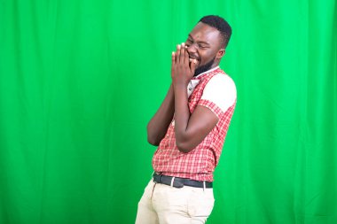 Yakışıklı, sakallı bir adam yeşil bir arka plan karşısında duruyor gülüyor ve elleriyle ağzını kapatıyor..