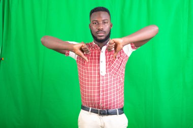 Yeşil arka planda duran, tişörtlü yakışıklı, sakallı bir adam memnuniyetsizlik jesti yapıyor..