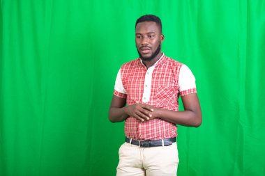 Tişörtlü, yeşil arka planda duran yakışıklı, sakallı bir adam stresli bir görünüm sergiliyor..