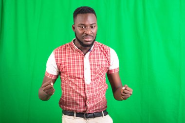 Yakışıklı, sakallı bir adam yeşil arka planda duruyor öfkeli bakışlarla yumruklar oluşturuyor..