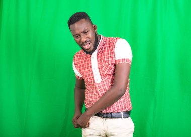 Yeşil arka planda duran ve cebinde bir şey arayan, tişörtlü, genç ve yakışıklı bir sakallı adam..