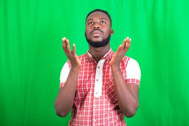 Yeşil bir arka planda duran, gömlekli, sakallı yakışıklı bir adam umutsuzluk içinde dua ediyor..