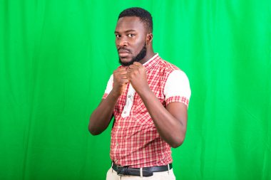 Yakışıklı, sakallı bir adam. Arka planda duruyor. Öfkeli bakışlarla yumruklar oluşturuyor..