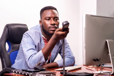 yakışıklı genç işadamı ofiste dizüstü bilgisayarın önünde oturuyor ve elinde bir cep telefonu var.