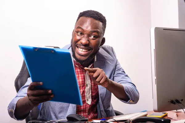 Joven Hombre Negocios Feliz Sentado Escritorio Señalando Dedo Portapapeles Mientras —  Fotos de Stock