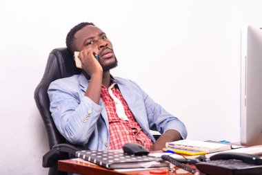 Ceketli iş adamı masasında oturmuş, cep telefonuyla karamsar bir bakışla konuşuyor..