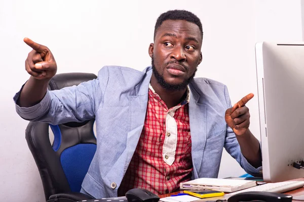 Genç iş adamı masada oturuyor ve bir parmağını bir yana, diğerini de bilgisayarın ekranında gösteriyor..