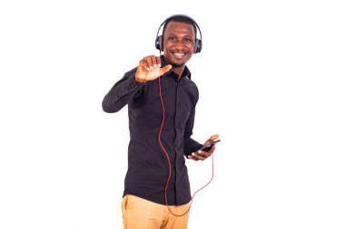 Beyaz bir arka planda duran, kulaklık ve cep telefonu kullanarak müzik dinleyen ve gülen bir öğrenci..