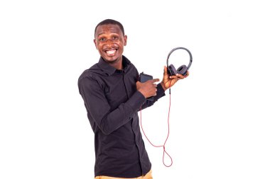 Beyaz arka planda duran bir öğrenci kameraya bakıp gülerken kulaklıkla işaret ediyor..