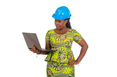 Güvenlik kaskı takan ve gülümserken dizüstü bilgisayarda çalışan güzel bayan mühendis..