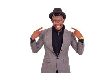 Yakışıklı genç bir işadamının portresi şık bir takım elbise giyiyor ve gülümserken parmaklarını yüzüne doğrultuyor..