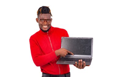 Yakışıklı genç adam kırmızı kazak giyiyor ve gülümserken bilgisayarı işaret ediyor..