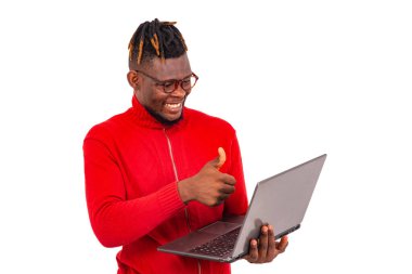 Kırmızı kazak giyen genç adam bilgisayardan ararken başparmağıyla gülümsüyor..