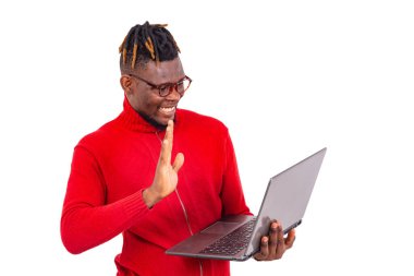 Genç adam kırmızı kazak giyiyor ve videoda gülümserken el sallıyor..