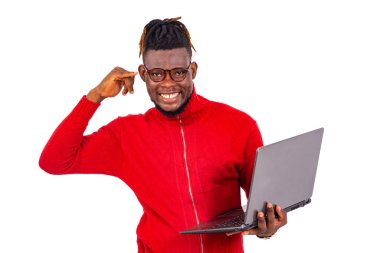 Kırmızı kazak giyen yakışıklı genç adam dizüstü bilgisayar tutuyor ve parmaklarıyla cep telefonu hareketi yapıyor..