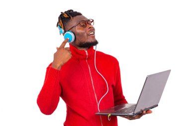 Saçları örgülü genç bir öğrenci beyaz arka plan karşısında dizüstü bilgisayar ve kulaklık kullanarak müzik dinliyor..