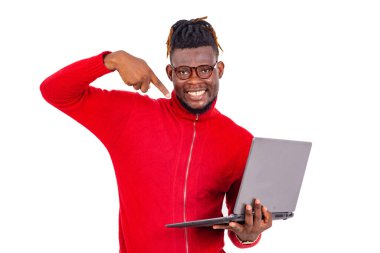 Yakışıklı genç adam kırmızı kazak giyiyor ve gülümserken bilgisayarı işaret ediyor..