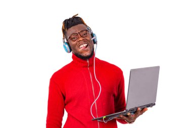 Saçları örgülü genç bir öğrenci beyaz arka plan karşısında dizüstü bilgisayar ve kulaklık kullanarak müzik dinliyor..