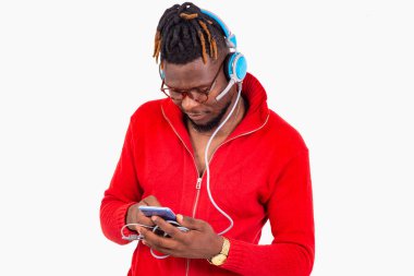 Beyaz arka planda duran gözlüklü genç bir adam cep telefonundan müzik dinliyor..