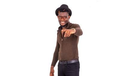 Şapkalı yakışıklı genç bir işadamı beyaz arka planda durup kameraya gülümserken işaret ediyor..