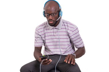 Genç adam sandalyede oturuyor ve telefon kulaklığıyla müzik dinliyor..